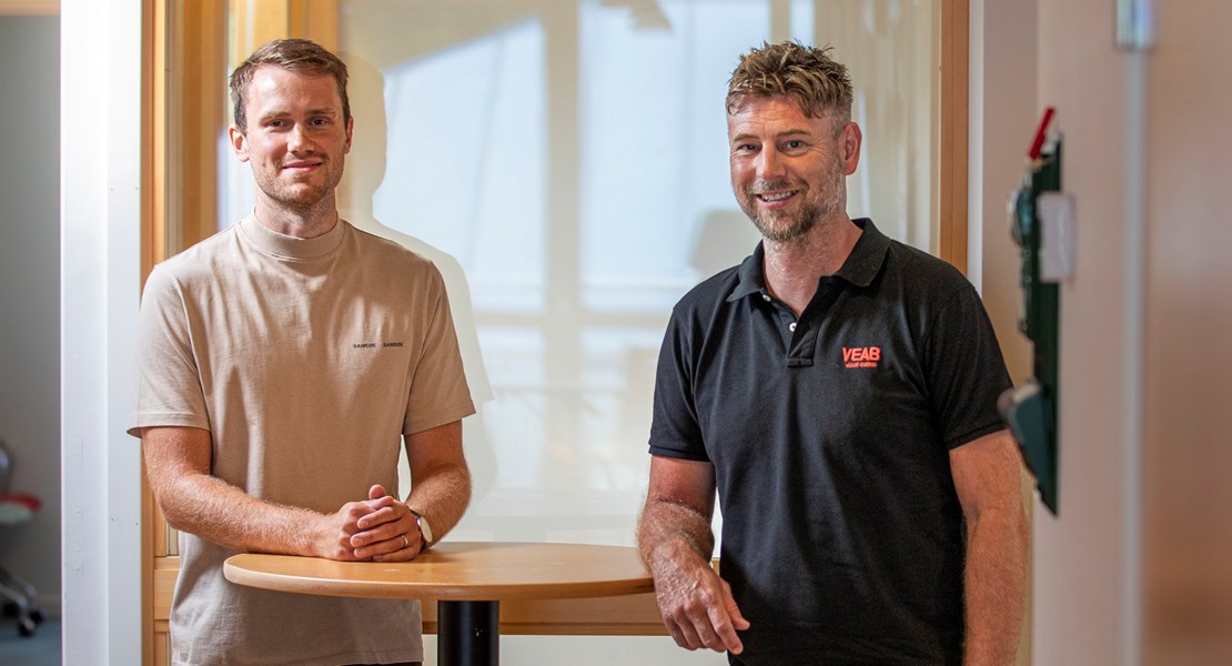 Martin och Johan står vid ett bord och tittar in mot kameran.