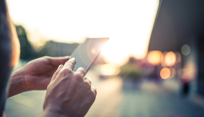 Närbild på mobil telefon som någon håller i med bakgrund i oskärpa