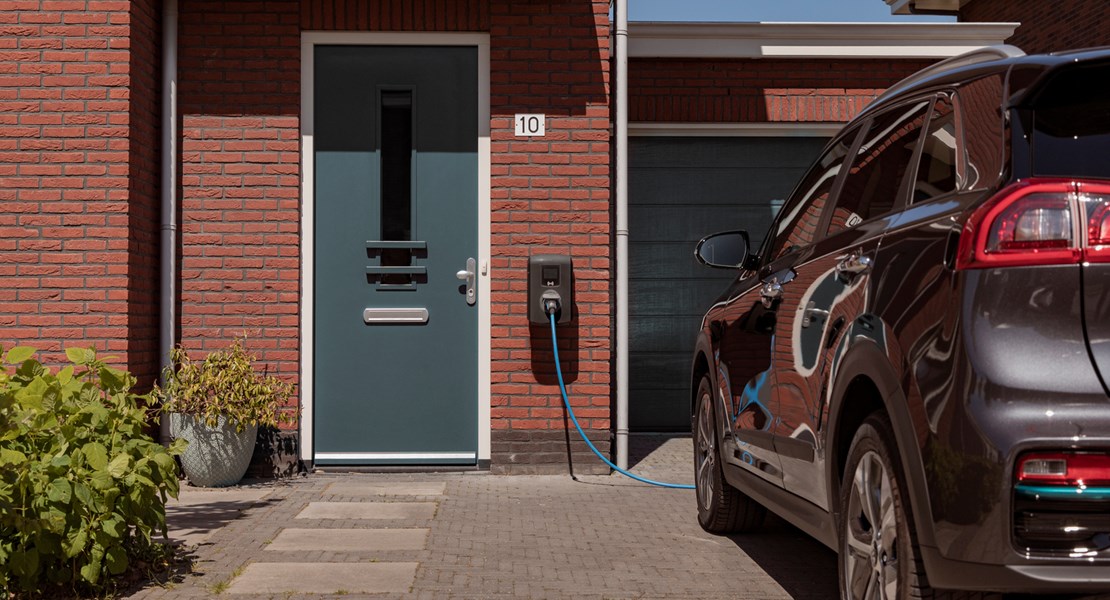 Elbil står parker på garageuppfart, inkopplad till laddbox
