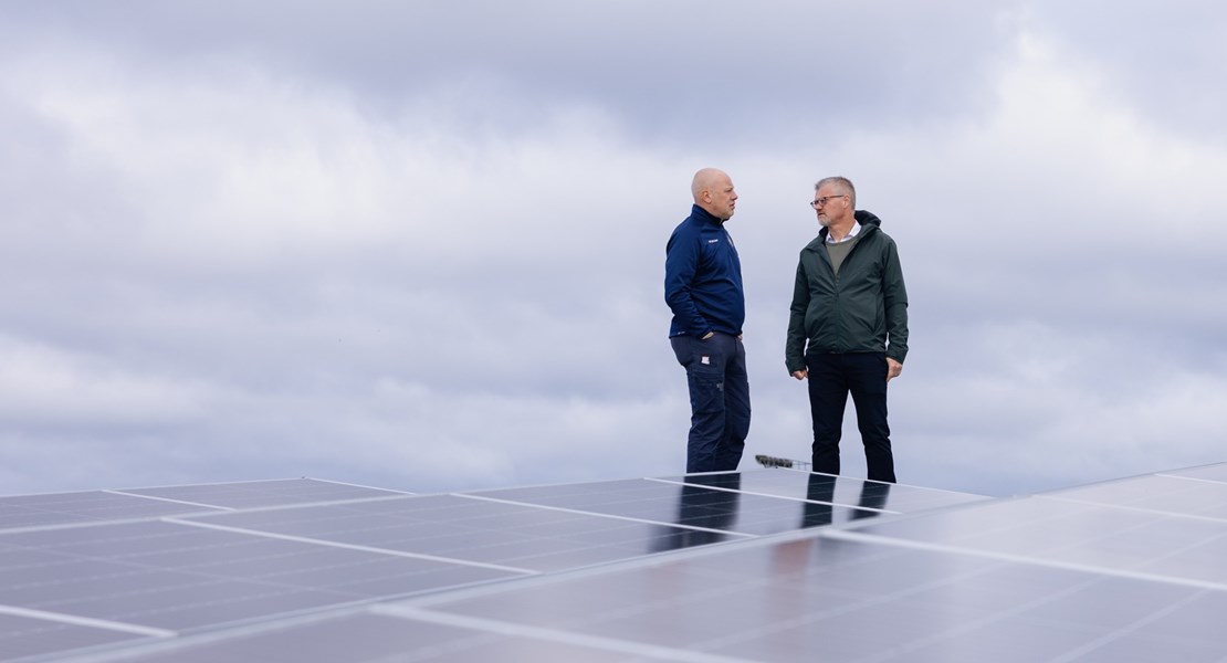 Två män står på fastighetens tak intill solpaneler